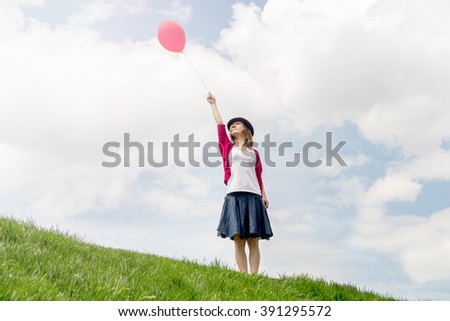 Happy girl holding air balloon on the green grass