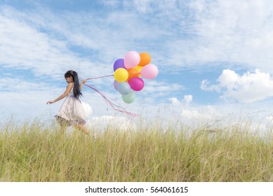Happy girl holding colorful of air balloons on a green meadow with cloudy and blue sky
