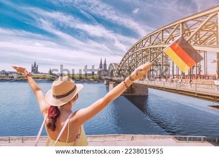 Happy girl holding a German flag against the Rhine bridge and Cologne Dom Cathedral. Travel landmarks and traditional holidays