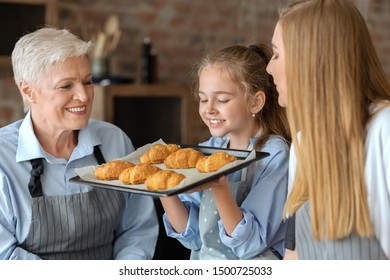 Happy Girl Holding Tray And Smelling Freshly Baked Croissants, Cooking With Mom And Granny, Kitchen Interior