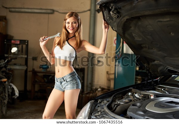 A\
happy girl holding a wrench poses near a black\
car.