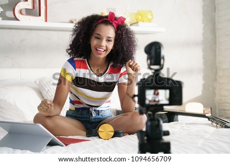 Happy girl at home speaking in front of camera for vlog. Young black woman working as blogger, recording video tutorial for Internet