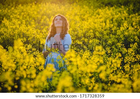 Happy girl hugs the bible in the sunlight on a background of yellow flowers. Girl with a book outdoors. Concept for faith, spirituality and religion. Peace, hope
