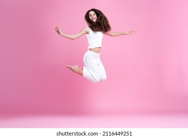 Happy girl jumping for joy, mid-air pose, sporty, active and energetic, pink background