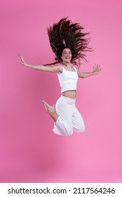 Happy girl jumping for joy, mid-air pose, sporty, active and energetic, pink background