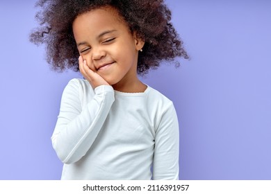Happy girl kid keeps hands on cheeks,smiles satisfied,amiably,with eyes closed, has fun chatting with friends, wears casual clothes, isolated over purple background.Good mood concept.Copy space. - Shutterstock ID 2116391957