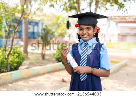 Happy girl kid in uniform standing by dreaming about graduation while holding graduation certificate at school - concept of future career, education and development.