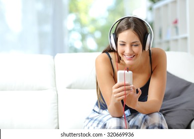 Happy girl listening music from smartphone with headphones in the living room at home