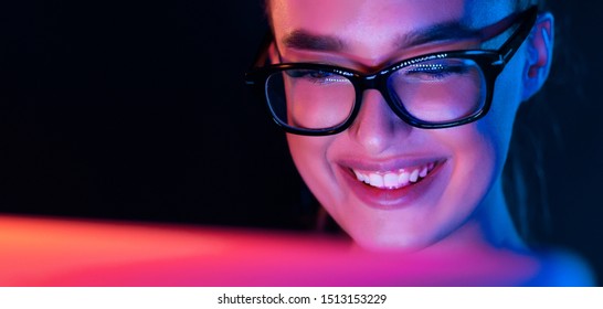 Happy Girl Looking At Laptop Screen At Night, Wearing Glasses, Face Illuminated By Neon Light, Free Space