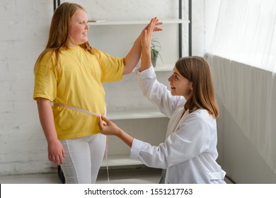 Happy Girl Losing Excess Weight. Nutritionist Measuring Her Waistline And Giving High Five To Her Young Patient.