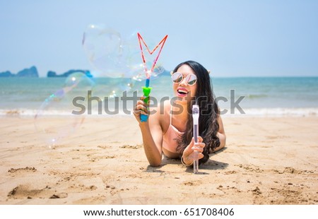 Happy girl making soap bubbles while lying on the beach