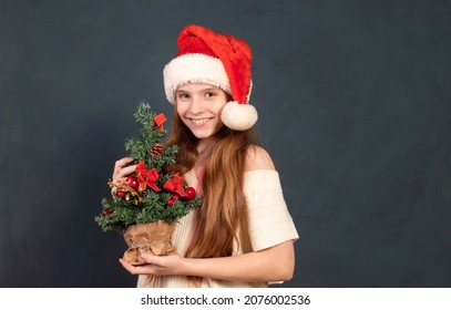 Happy Girl In A New Year Cap For Christmas With A Tree In Her Ha