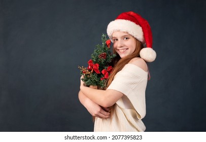 Happy Girl In A New Year Cap For Christmas With A Tree In Her Ha