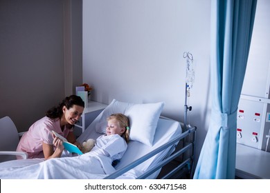 Happy girl on a bed reading book with her mother in hospital - Powered by Shutterstock