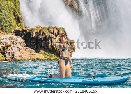 Happy girl on a SUP board near huge Duden waterfall in Antalya, Turkey. Summer watersports and recreation and adventure concept
