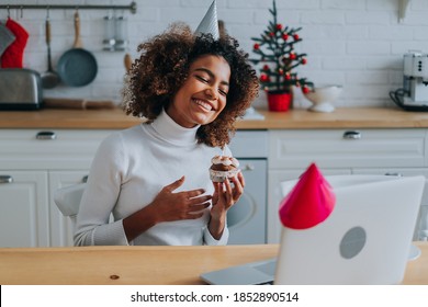 Happy girl with perfect dark skin and trendy kinky hair holding birthday cupcake and posing against modern laptop closeup - Powered by Shutterstock