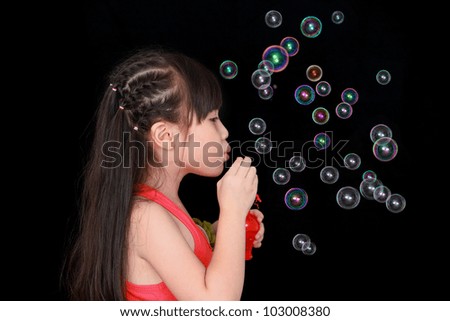 Happy girl play with soap bubbles isolated black background