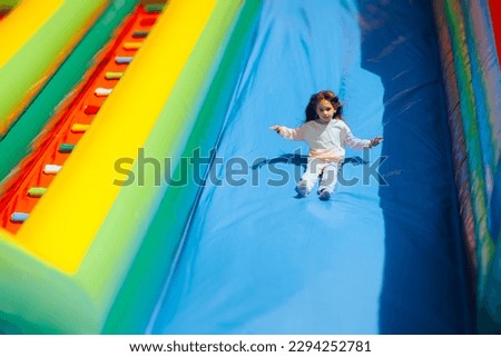 
Happy Girl Playing on a Huge Inflatable Slide in Amusement Park. Cheerful carefree child having fun in a bouncing castle 
