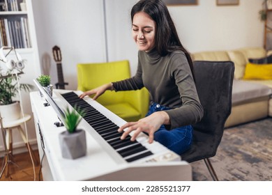 Chica feliz está tocando piano para su pasatiempo de relajarse en la sala de estar de su casa. Retrato De Una Joven Sonriente En Casa Jugando El Piano