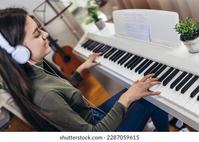 Happy girl is playing piano for her hobby relax time in home living room. Portrait Of Smiling Teenage Girl At Home Playing The Piano - Powered by Shutterstock