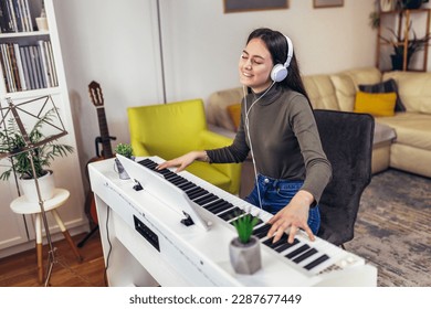 Happy girl is playing piano for her hobby relax time in home living room. Portrait Of Smiling Teenage Girl At Home Playing The Piano - Powered by Shutterstock