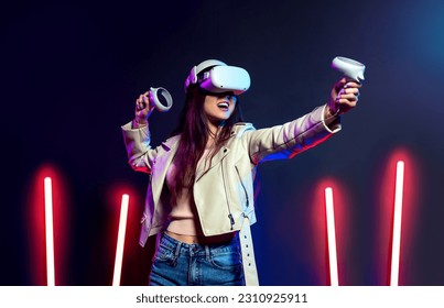 Happy girl playing virtual reality game in vr headset glasses in neon lights. Gamer in goggles with joysticks. - Shutterstock ID 2310925911