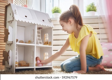 Happy girl plays with doll house and teddy bear at home. Funny lovely child is having fun in kids room.