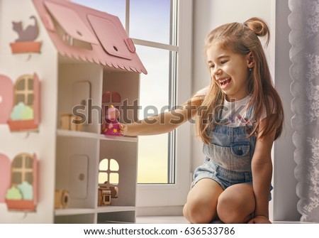 Happy girl plays with doll house and teddy bear at home. Funny lovely child is having fun in kids room.