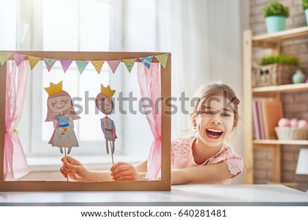 Happy girl plays with performance in the puppet theater with prince and princess at home. Funny lovely child is having fun in kids room.