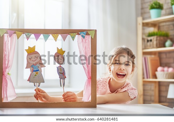 Счастливая девушка играет с выступлением в кукольном театре с принцем и принцессой дома. Забавный прекрасный ребенок имеет удовольствие в детской комнате.