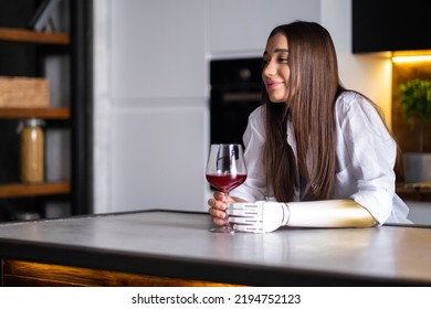 Happy Girl With Prosthetic Arm Holds Glass Of Wine In Artificial Prosthetic Limb Hand At Home