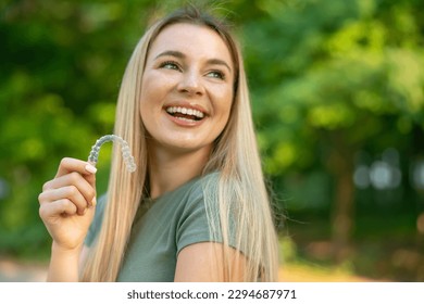 Happy girl puts a dental retainer on her teeth, she stands on a green background. Orthodontist. Dental tray. Retainer. Place for an inscription. - Powered by Shutterstock