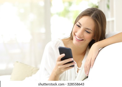 Happy Girl Reading A Message In A Smart Phone Sitting On A Couch At Home