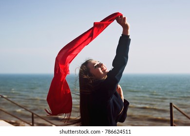 Happy girl with a red shawl waving in the wind near the sea shore - Powered by Shutterstock