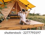 Happy girl relaxing on vacation. Camping young woman sitting in camp tent. Young female caucasian model reading text and work on notebook