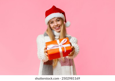 Happy girl in Santa hat giving Christmas present, yellow studio background, empty space - Powered by Shutterstock