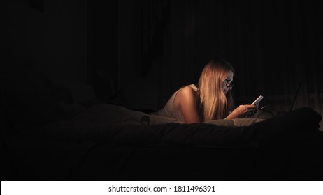 Happy Girl Selecting And Watching Video In A Smart Phone Lying On The Bed In The Night At Home