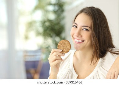Happy girl showing a dietetic cookie sitting on a couch at home