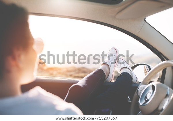 Happy girl is sitting in the car and pushes her\
shoes out of car to enjoy the\
view.