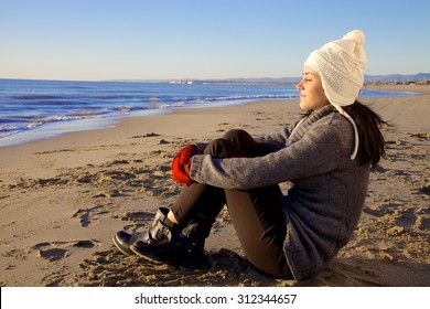 Happy Girl Sitting On Beach In Winter