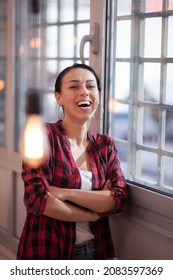 Happy girl with smiling and looking at camera next to a window in a modern coworking office space. - Shutterstock ID 2083597369