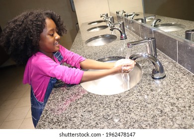 Happy girl smiling while washing hands in public restroom