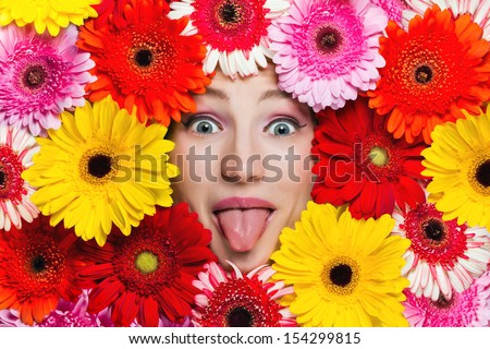 Happy girl sticking out tongue. Beautiful girl with gerbera daisy flowers around her face 