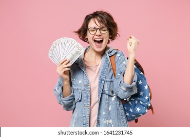 Happy Girl Student In Denim Clothes Glasses Backpack Isolated On Pastel Pink Background. Education In School University College Concept Hold Fan Of Cash Money In Dollar Banknotes Doing Winner Gesture