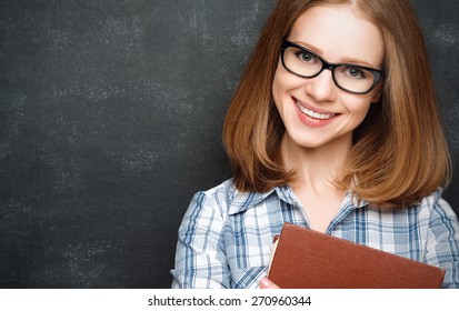 Happy Girl Student With Glasses And A Book From The  Blackboard