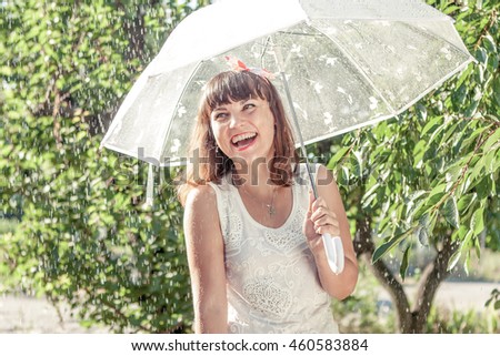Happy girl in the summer sunny rain. Funny young woman playing outdoors hot day with umbrella. Joyful emotions