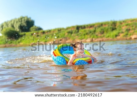 Happy girl swims on an inflatable circle in the river in summer at sunset. A child enjoys a summer children's holiday on the shore of the lake. Active holidays. Dynamic image