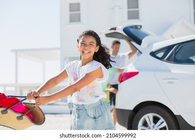 Happy girl swinging beach bag outside car in sunny driveway
