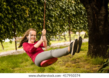 Happy girl swinging on seesaw hanging from cherry tree behind family house