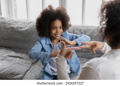 Happy girl talks to disabled deaf mom. Mother teaches kid sign language, shows hand gestures and finger symbols. Tutor giving lesson to positive child with hearing disability at home. Children therapy